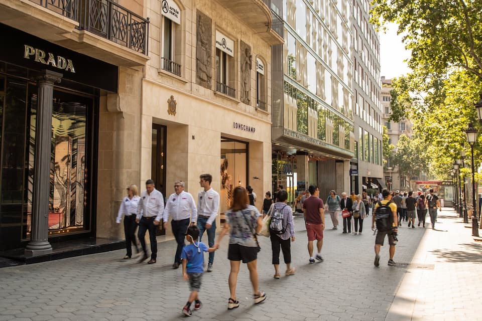 Une rue animée en plein centre-ville, bordée de boutiques de luxe comme Prada et Longchamp, où les piétons se promènent sur le trottoir.