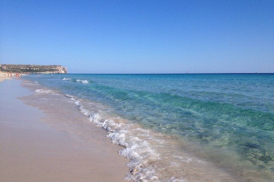 Una playa arenosa con agua turquesa cristalina y un acantilado lejano.