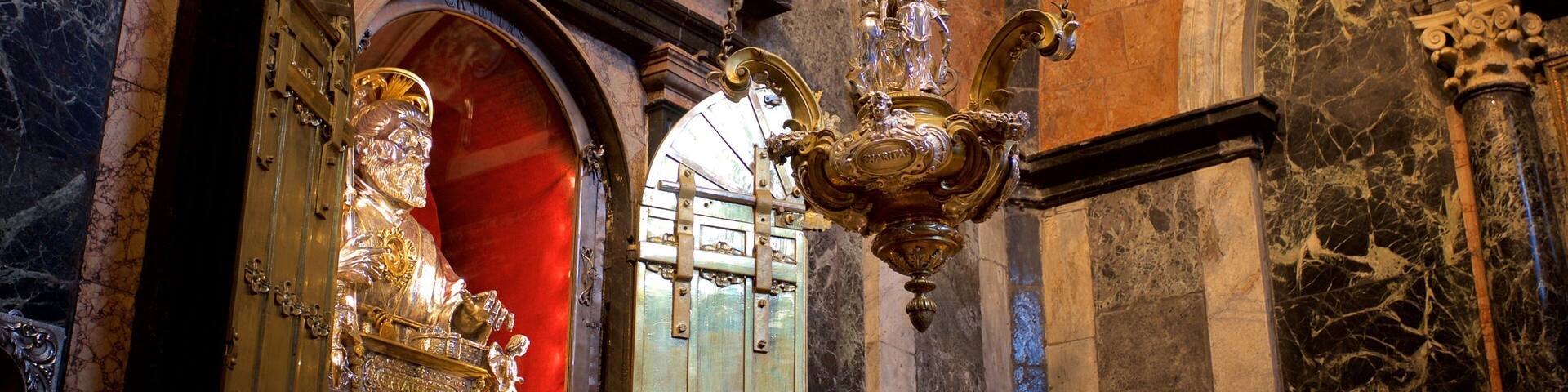 An ornate chandelier, marble walls, and a statue in a grand interior.