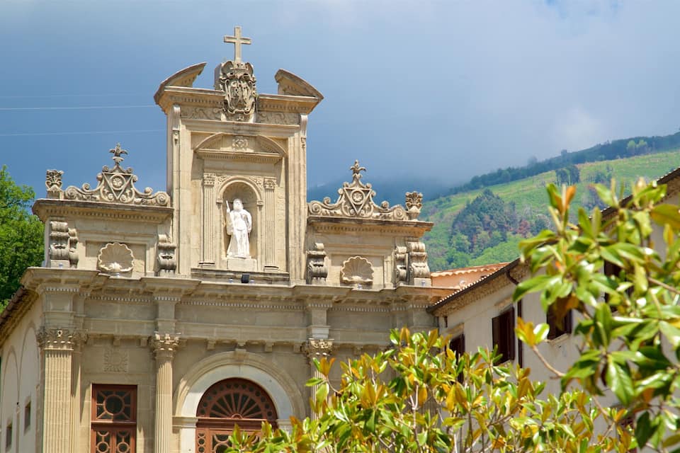 A church with a statue of a saint, ornate architecture, and a cross on top.
