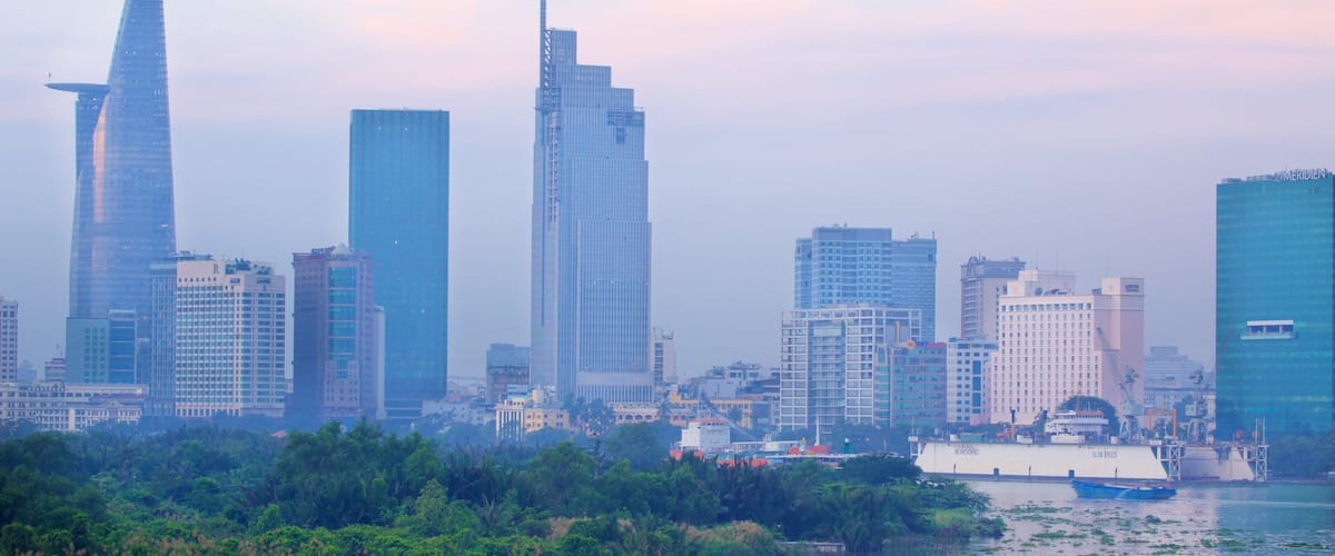 A city skyline with modern skyscrapers and a river with boats.