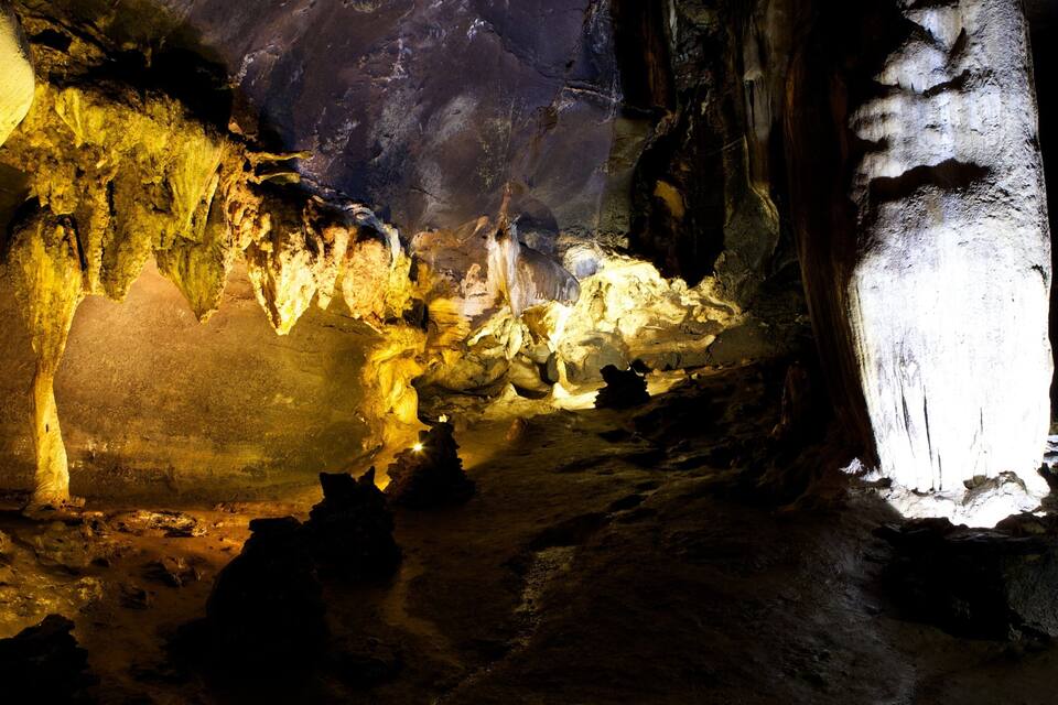 A cave with stalactites and stalagmites, illuminated by artificial lighting.