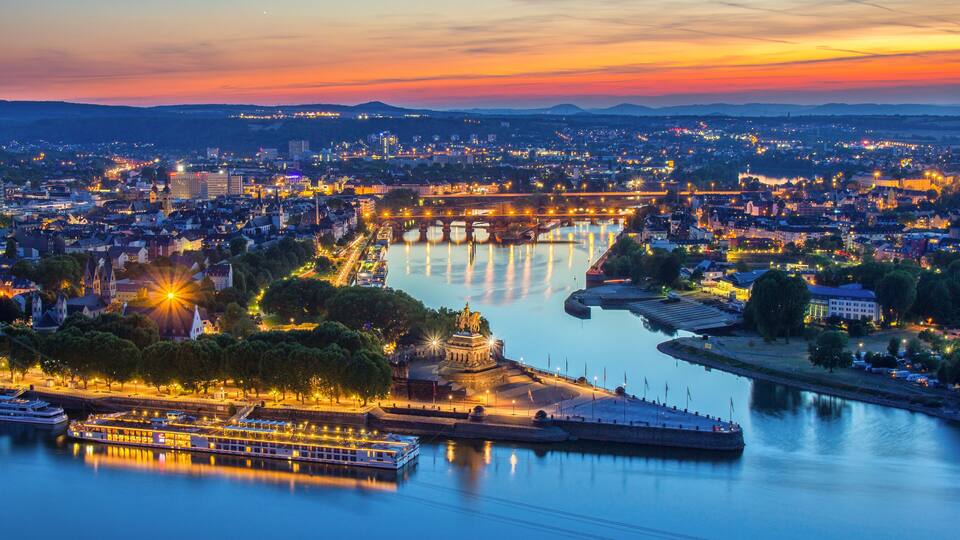 Una ciudad ribereña al atardecer, con puentes iluminados y un monumento histórico.