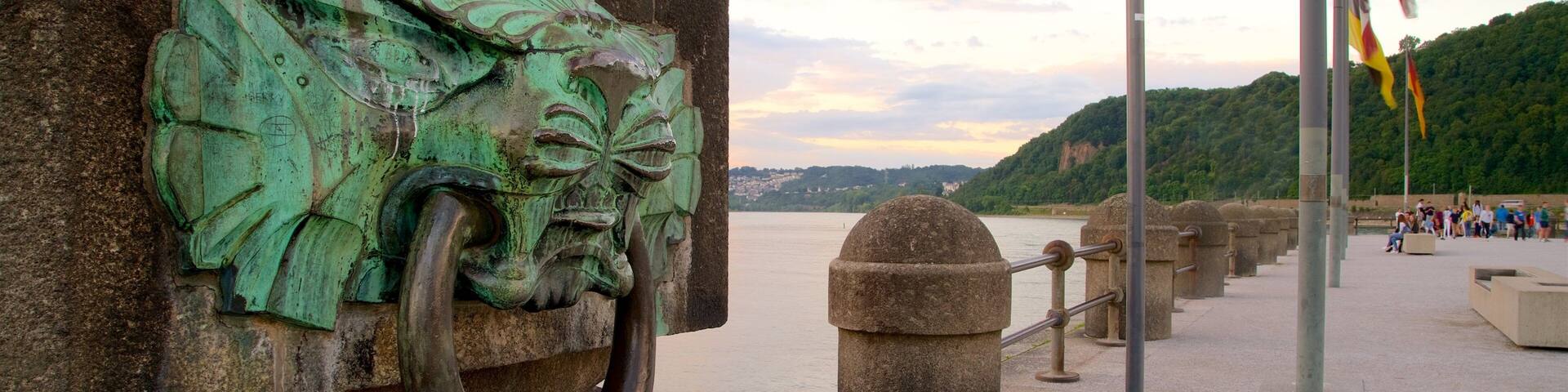 A stone monument with a greenish metal sculpture, a waterfront, and flags.