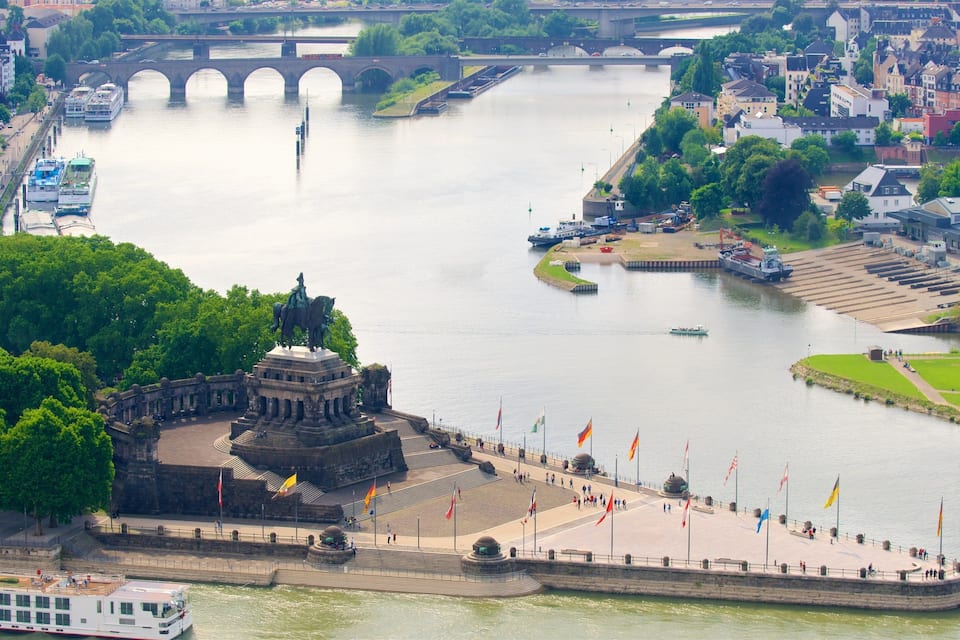 Ein Fluss mit einer Brücke, einer Statue und einer Uferpromenade mit Flaggen.