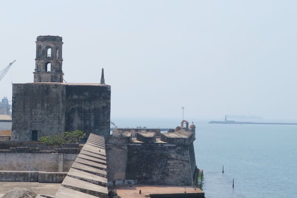 A historic fort with a bell tower, a ramp leading to the entrance, and a calm sea in the background.
