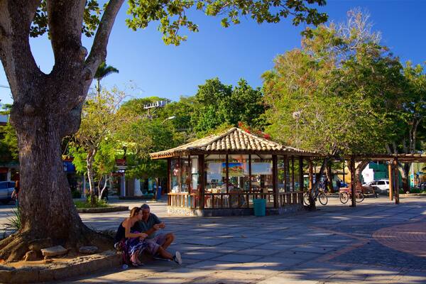 A gazebo in a park with a large tree and a couple sitting on the ground.