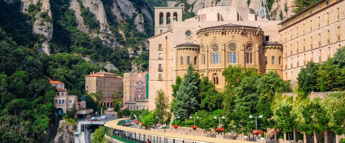 A historic building with a dome and arches, surrounded by a lush green park and towering rock formations.