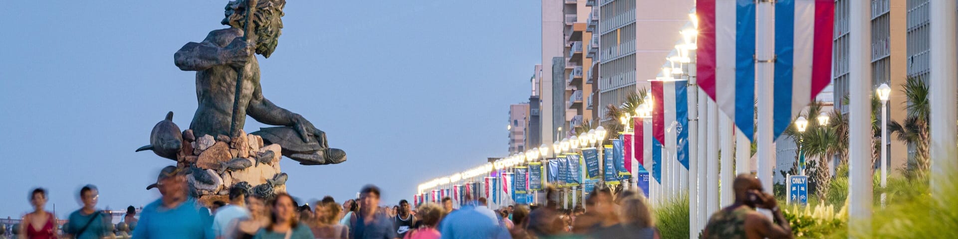 A busy pedestrian area with a statue of a figure holding a trident, surrounded by people.