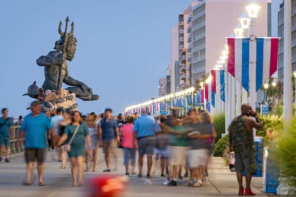 A busy pedestrian area with a statue of a figure holding a trident, surrounded by people.