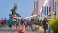 A busy pedestrian area with a statue of a figure holding a trident, surrounded by people.