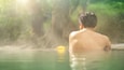 Asian man relaxing in morning is beautiful fog steam hot spring with sunlight at Hin Dat Hot Spring , Kanchanaburi , Thailand