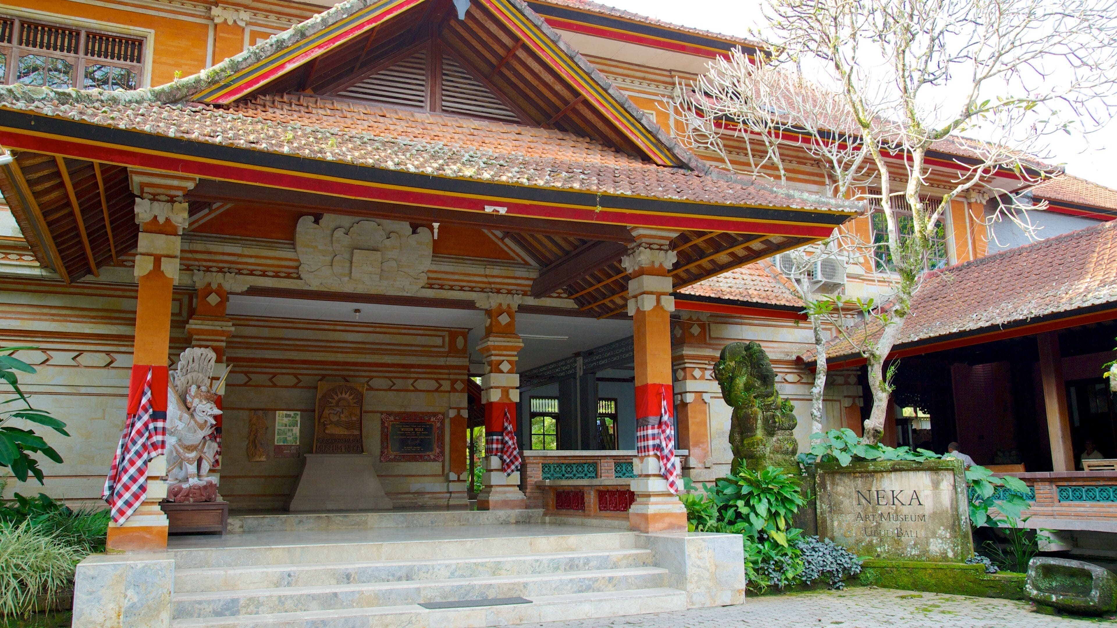 A traditional Balinese building with a tiled roof, ornate columns, and a statue.