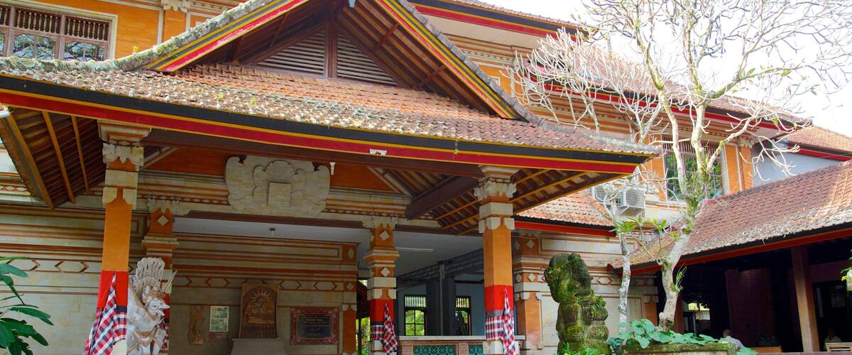 A traditional Balinese building with a tiled roof, ornate columns, and a statue.