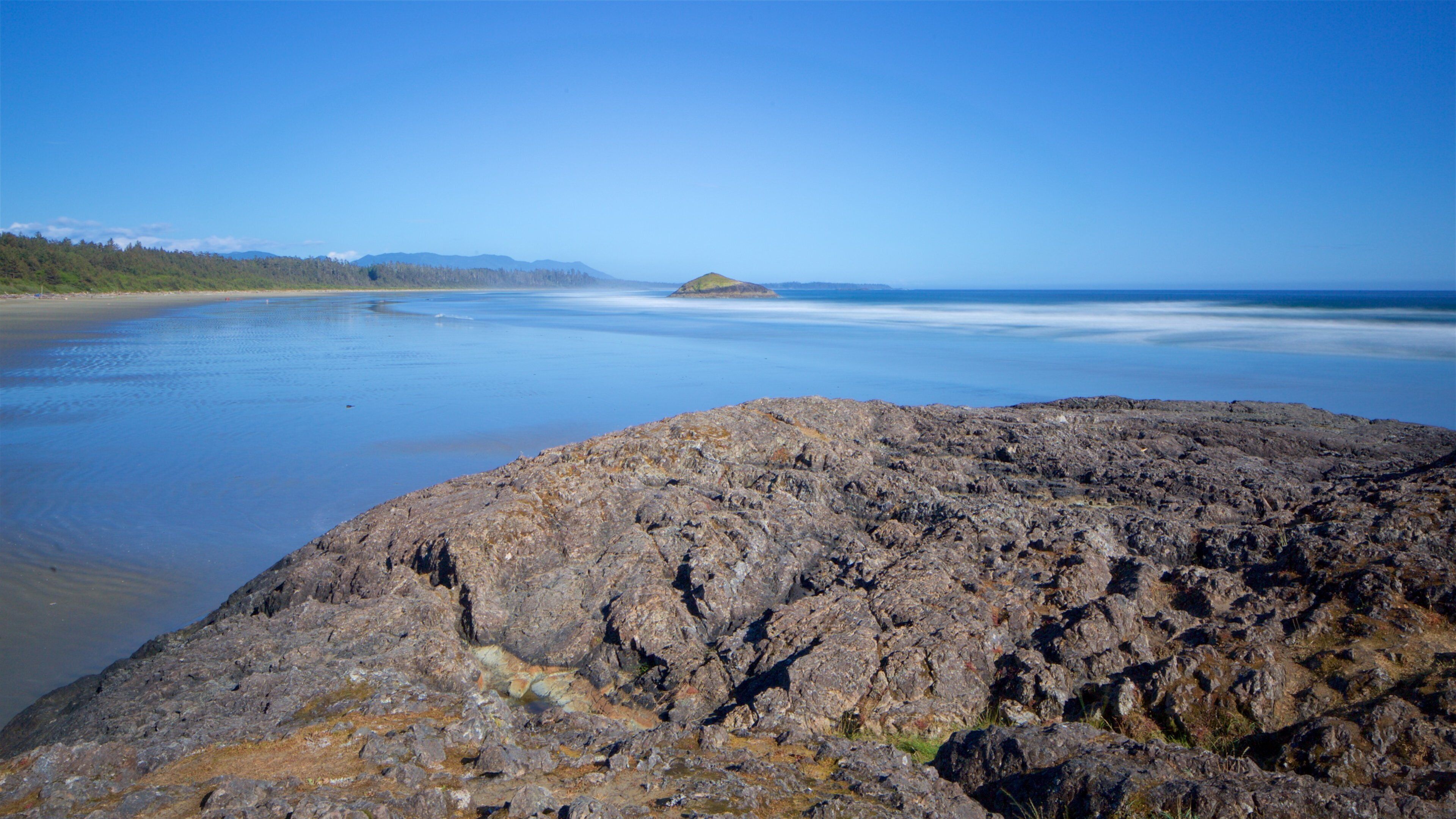 A rocky shoreline with calm water and distant mountains.