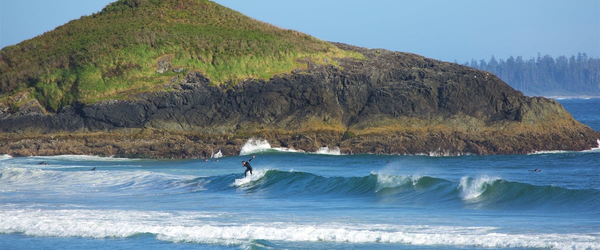 A rocky island with a grassy hill and a surfer riding a wave.