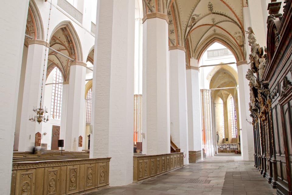 A grand cathedral interior with high vaulted ceilings, large stained glass windows, and ornate woodwork.