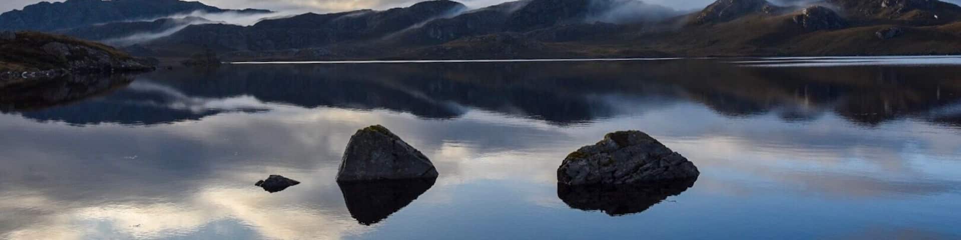 A calm lake with mountains in the background and a clear sky.