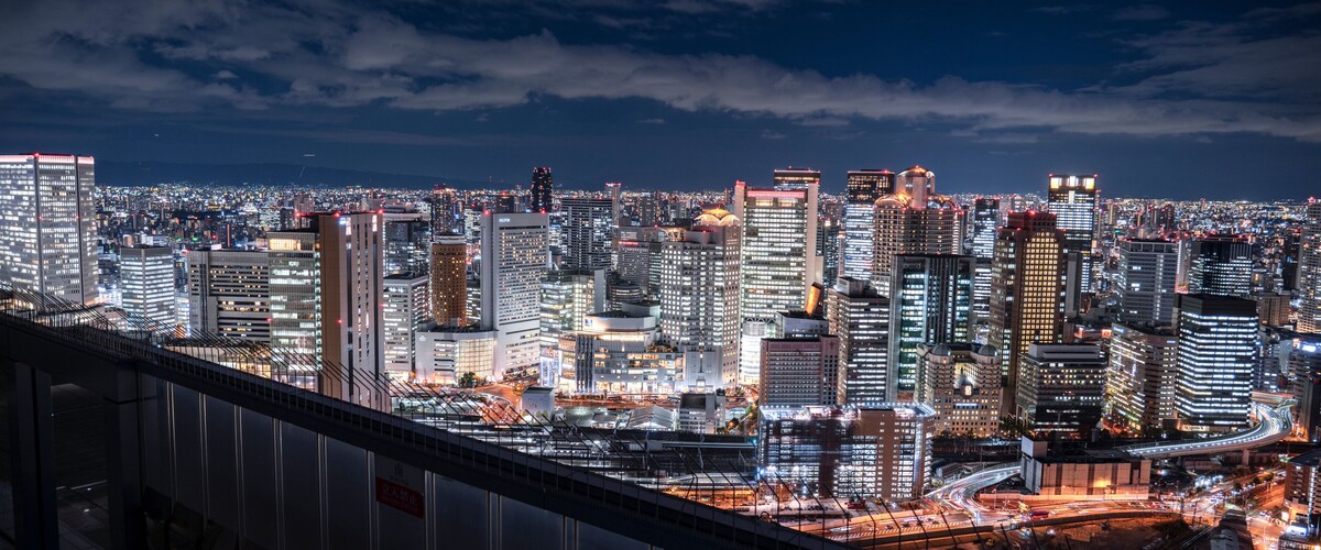 A nighttime cityscape with illuminated skyscrapers and a bridge in the foreground.