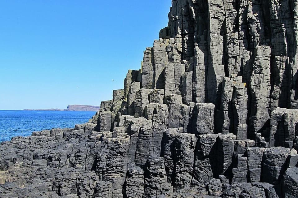 A rocky coastline with layered cliffs and the ocean in the background.