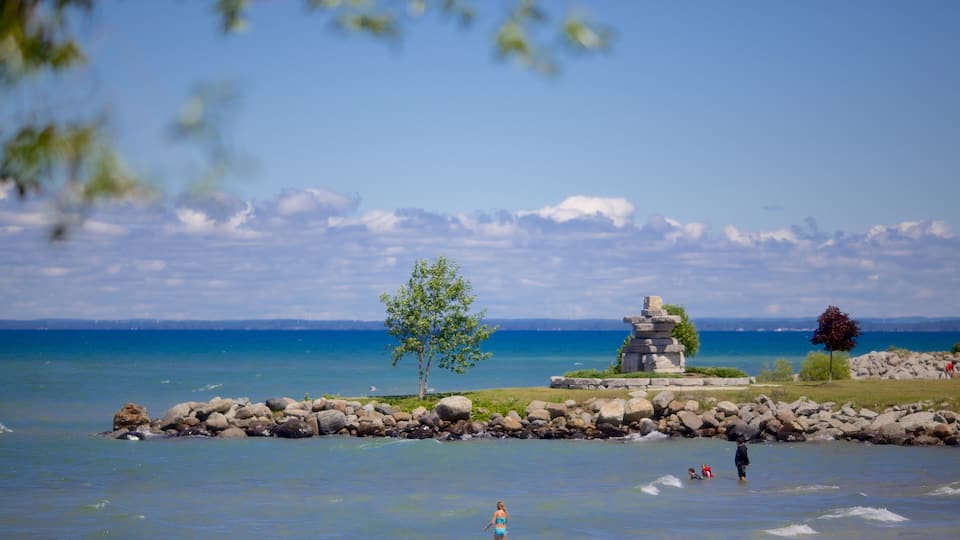 A clear blue lake with a rocky shoreline, a small stone monument, and a lone tree.