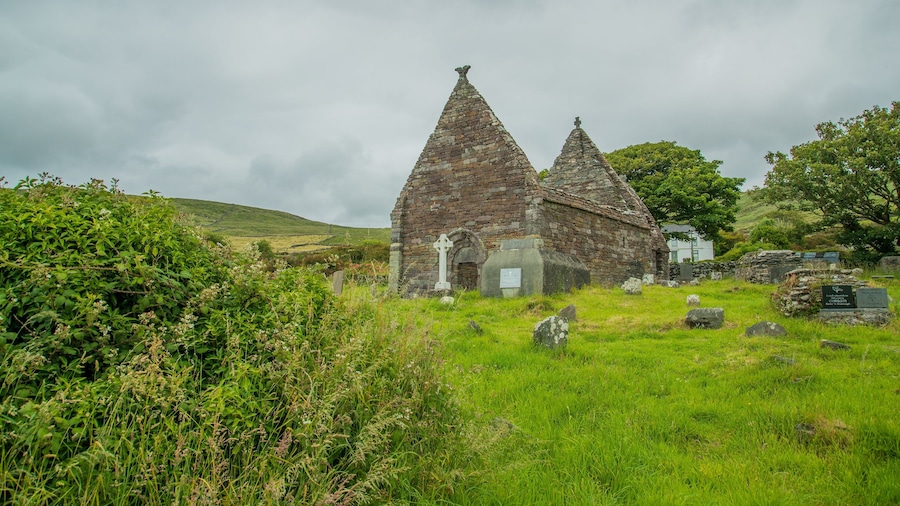 Una iglesia de piedra con dos torres puntiagudas y una cruz en la parte superior, rodeada de césped y árboles.