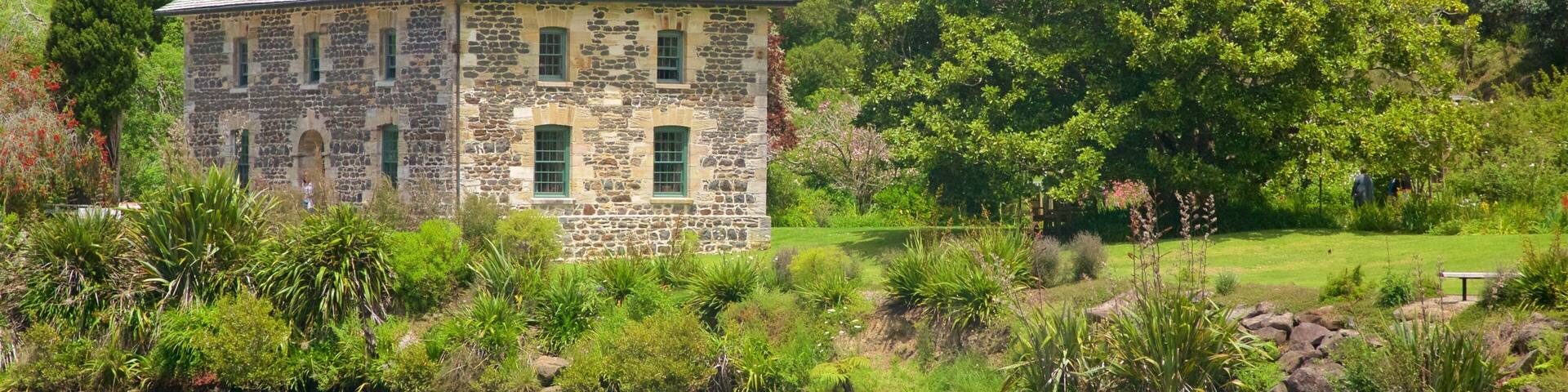 A stone house with a green roof by a lake, surrounded by lush greenery and trees.