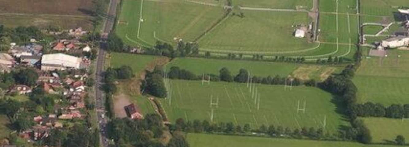 An aerial view of a rural area with a large football field, surrounding houses, and a small village.