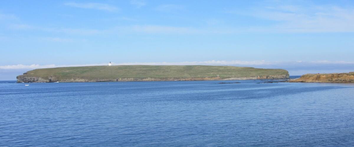 A coastal landscape with a lighthouse on a grassy hill, calm sea, and clear sky.