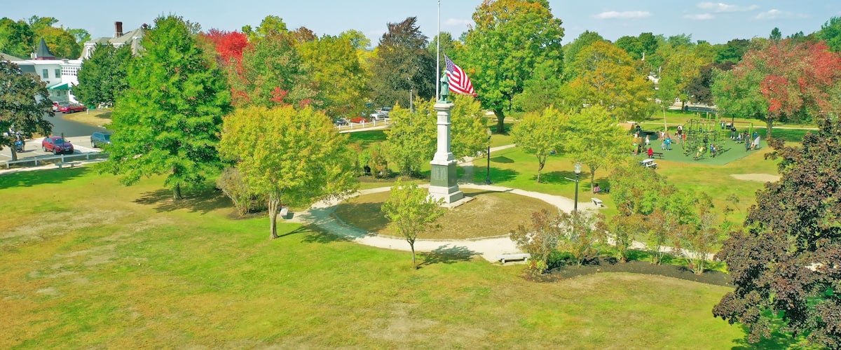 A park with a flagpole, trees, and a monument.