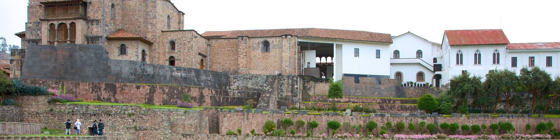 Un sitio histórico con un amplio muro de piedra, un campo cubierto de césped y lápidas, y una iglesia destacada al fondo.