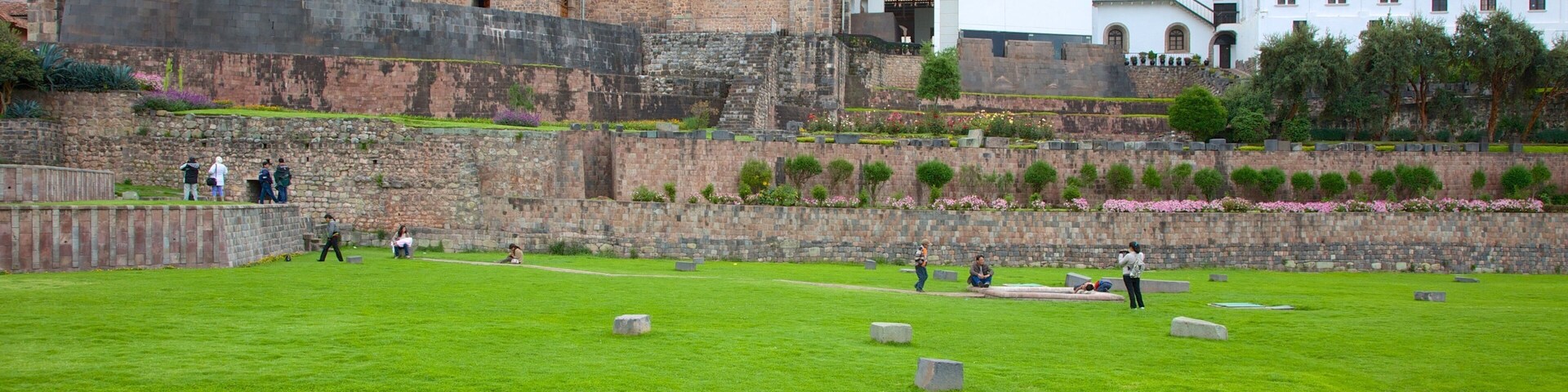 A historic site with a large stone wall, a grassy field with headstones, and a prominent church in the background.