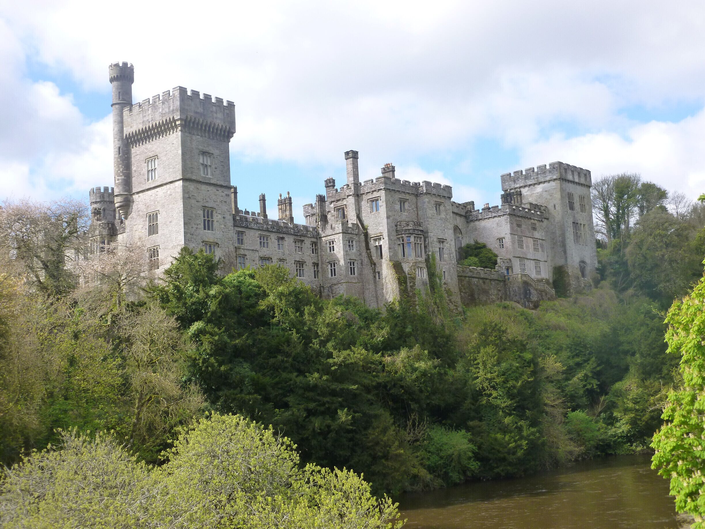 A large castle surrounded by dense greenery and a river.
