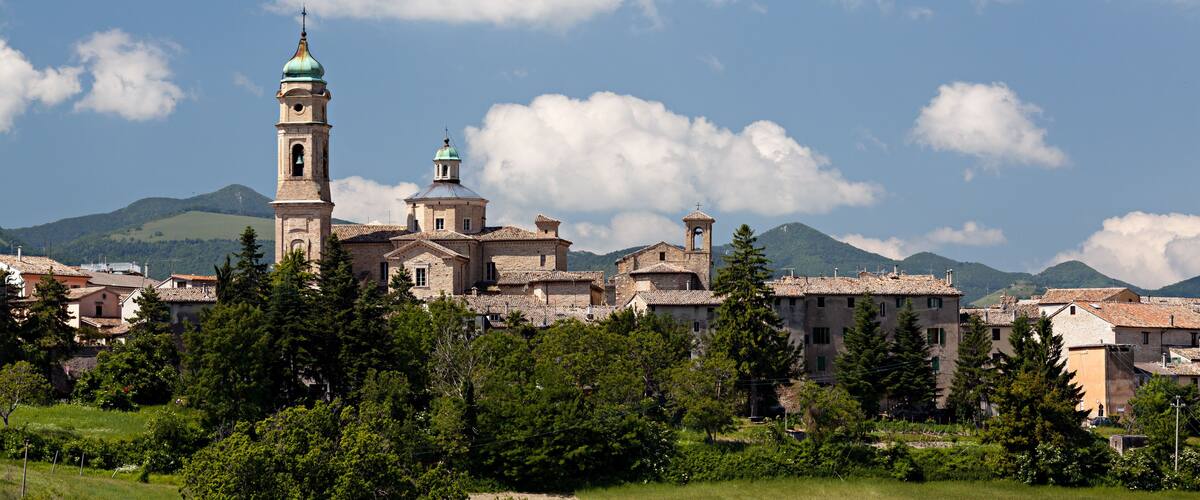 A historic town with a prominent church featuring a bell tower and green dome, surrounded by lush greenery and mountains in the background.