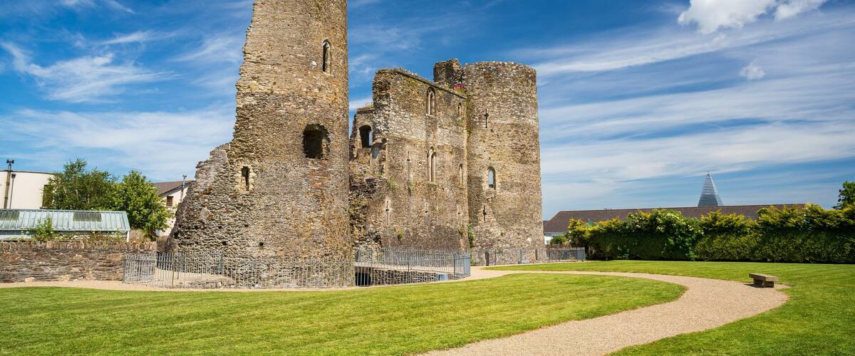 A historic stone castle with a tall tower, surrounded by a well-maintained lawn and a metal fence.