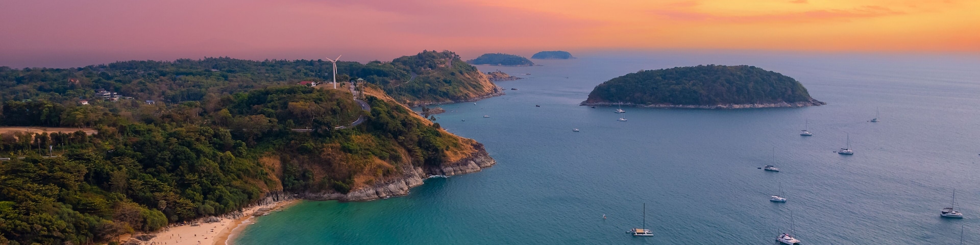 Un paisaje costero con playa, barcos y una turbina eólica.