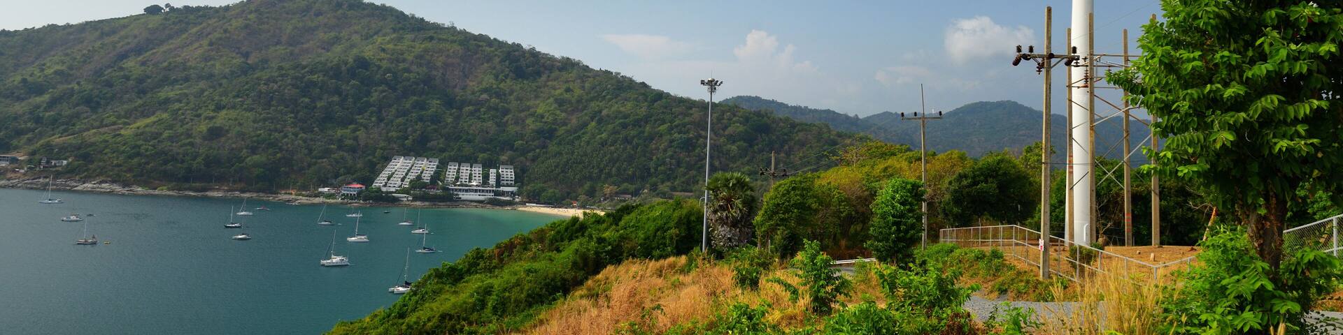 A wind turbine, a coastal bay with boats, and a hilly landscape.