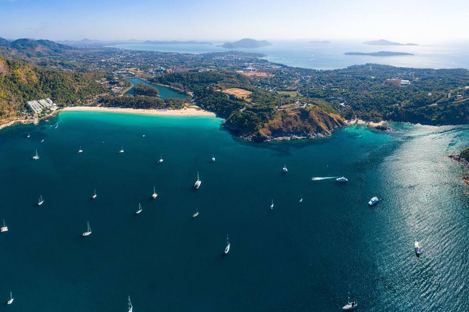 An aerial view of a coastal landscape with multiple islands, clear turquoise waters, and numerous sailboats.