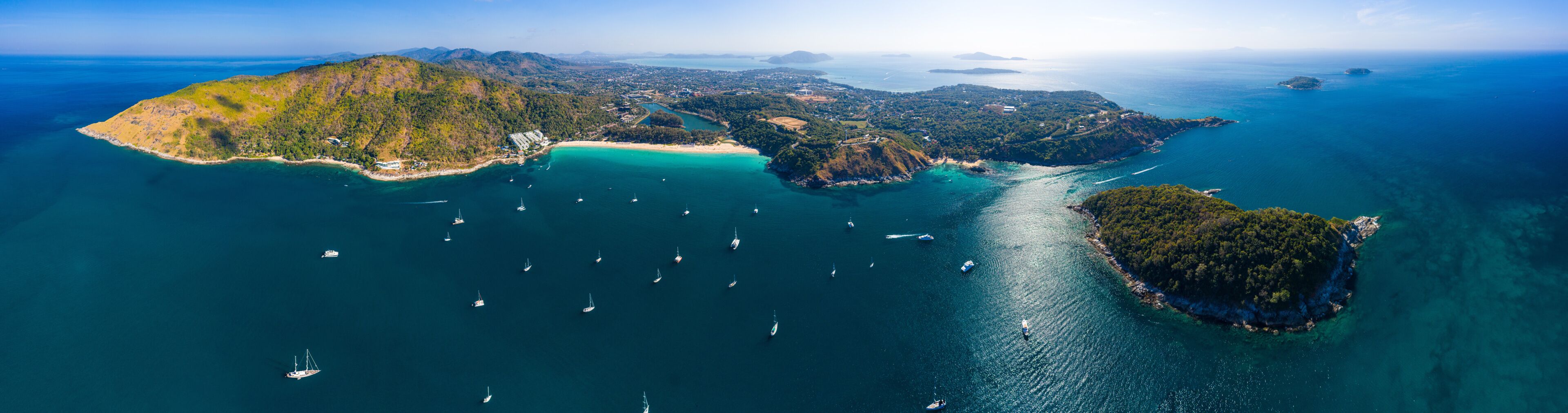 An aerial view of a coastal landscape with multiple islands, clear turquoise waters, and numerous sailboats.