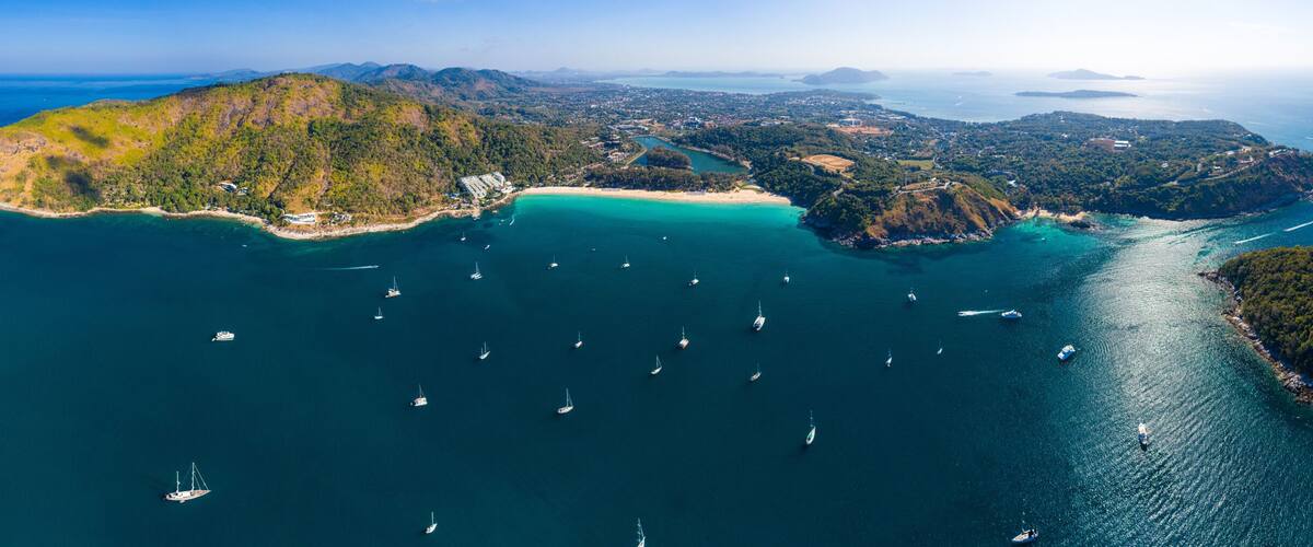 An aerial view of a coastal landscape with multiple islands, clear turquoise waters, and numerous sailboats.