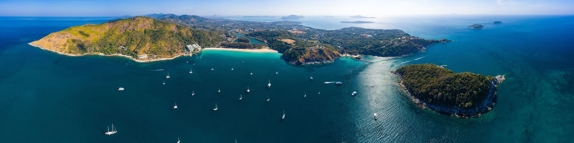 An aerial view of a coastal landscape with multiple islands, clear turquoise waters, and numerous sailboats.