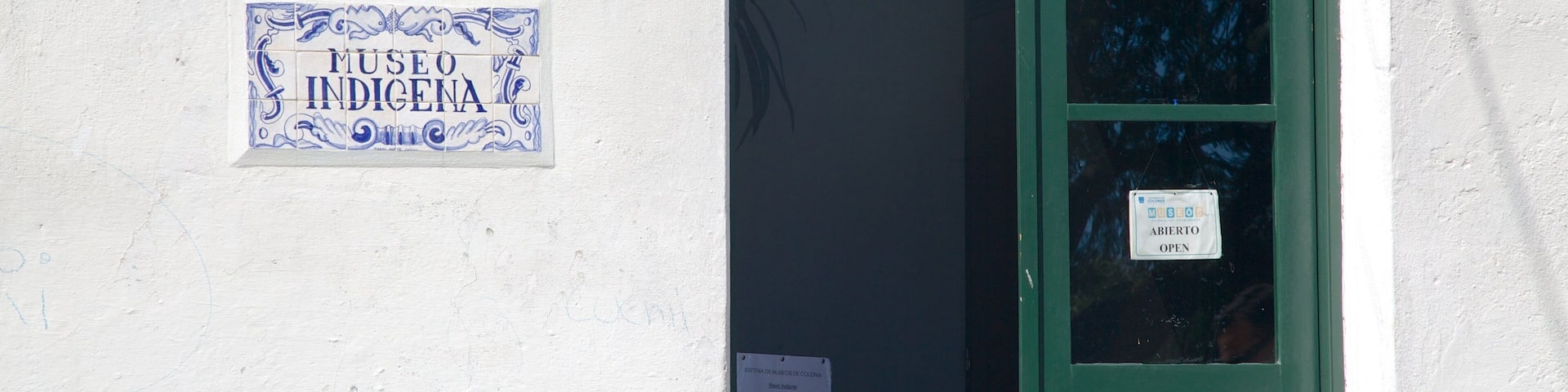 A white wall with a blue and white sign reading "Museo IndÃgena" and a green door with a sign that says "Museo Abierto."