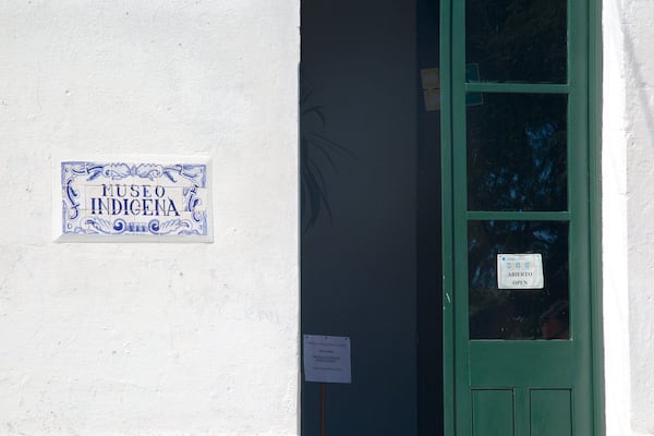 A white wall with a blue and white sign reading "Museo Indígena" and a green door with a sign that says "Museo Abierto."
