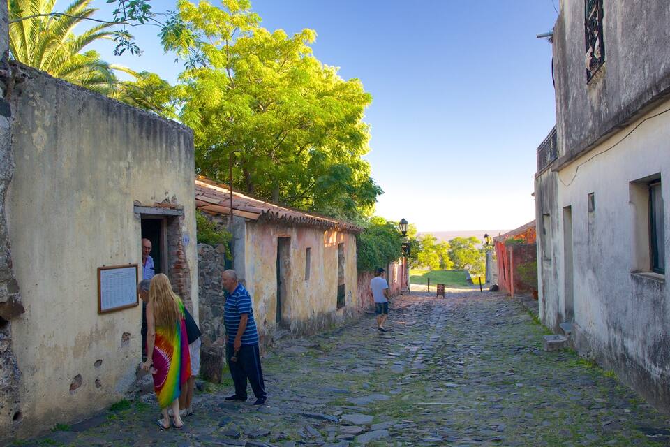 Ruas de paralelepípedos ladeadas por edifícios antigos, uma placa de sinalização e um lampião.