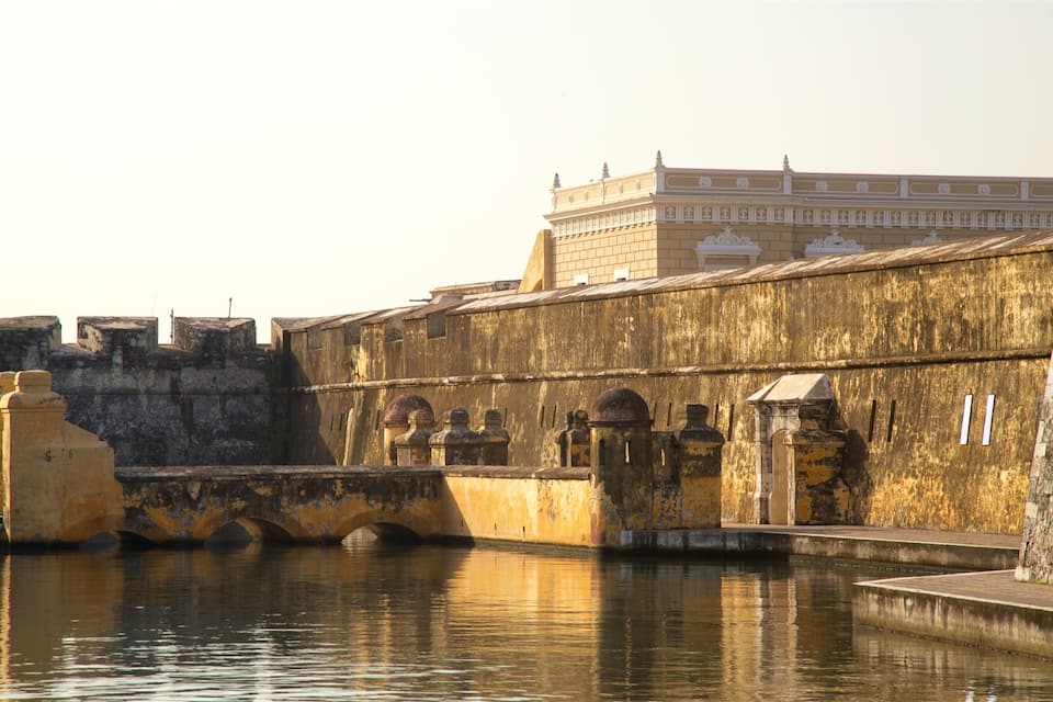 Una fortaleza histórica con un puente sobre el agua, reflejando la estructura y un edificio en el fondo.