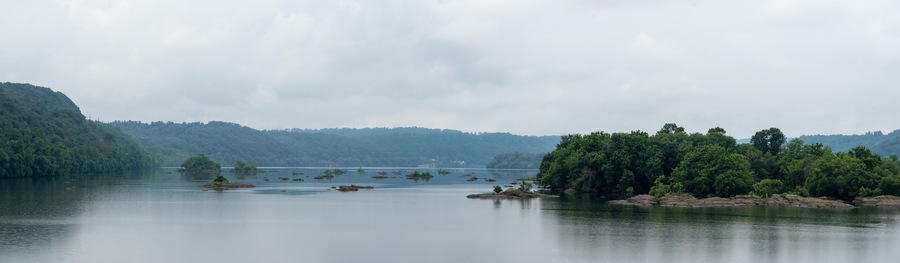 A calm lake with several small islands and dense forested hills in the background.