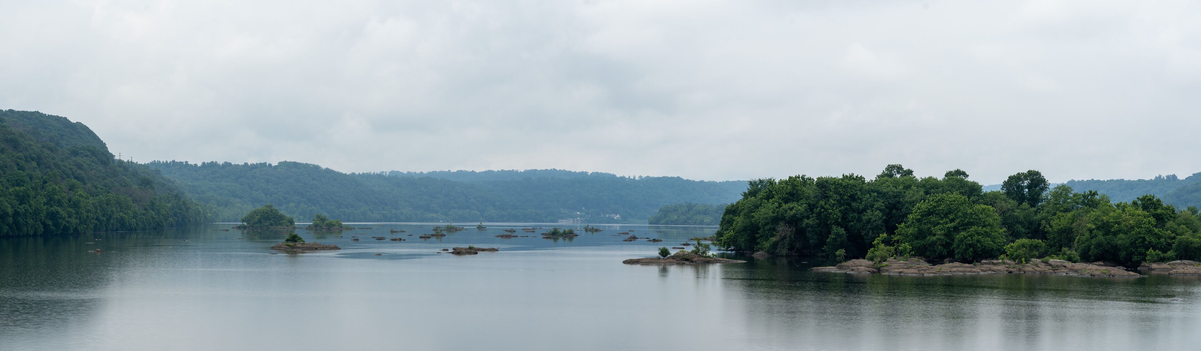 A calm lake with several small islands and dense forested hills in the background.