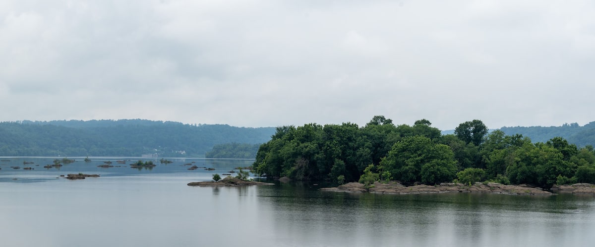 A calm lake with several small islands and dense forested hills in the background.