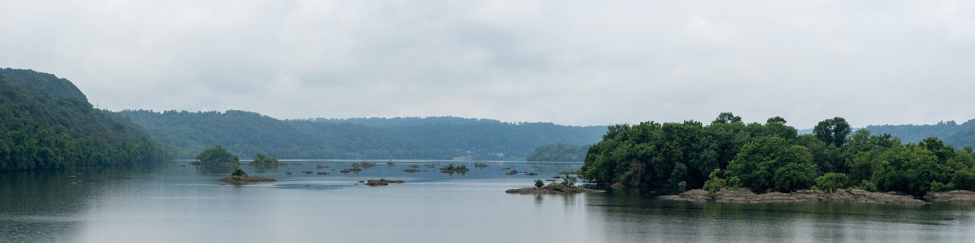 A calm lake with several small islands and dense forested hills in the background.