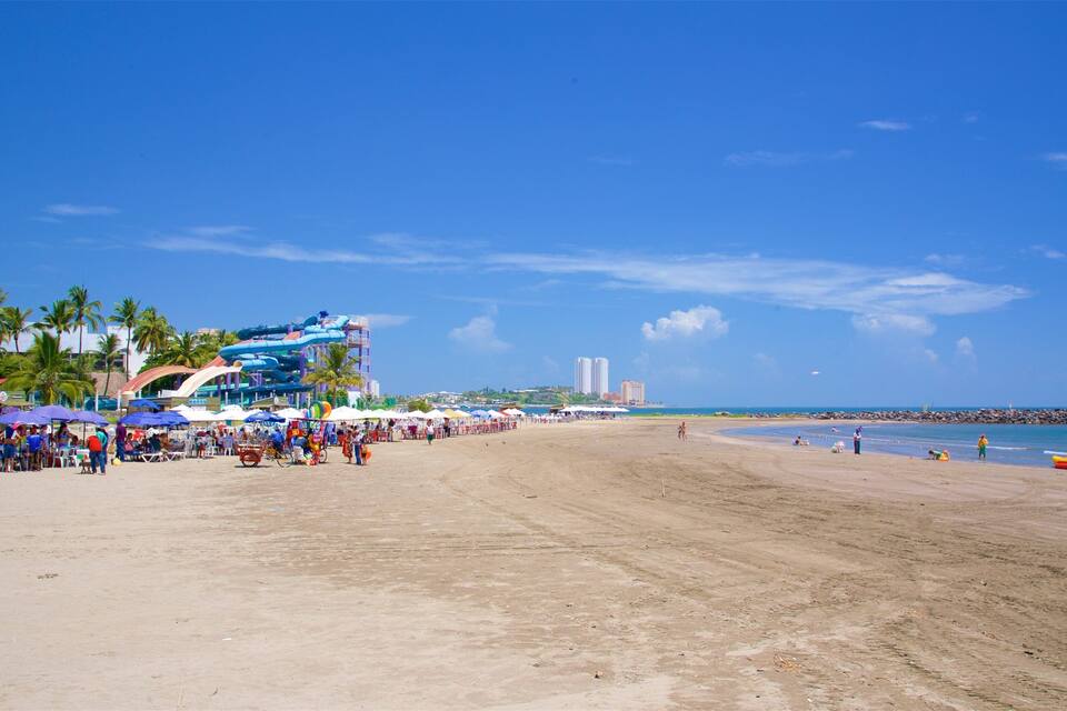 A beach with a water park, palm trees, and a clear blue sky.